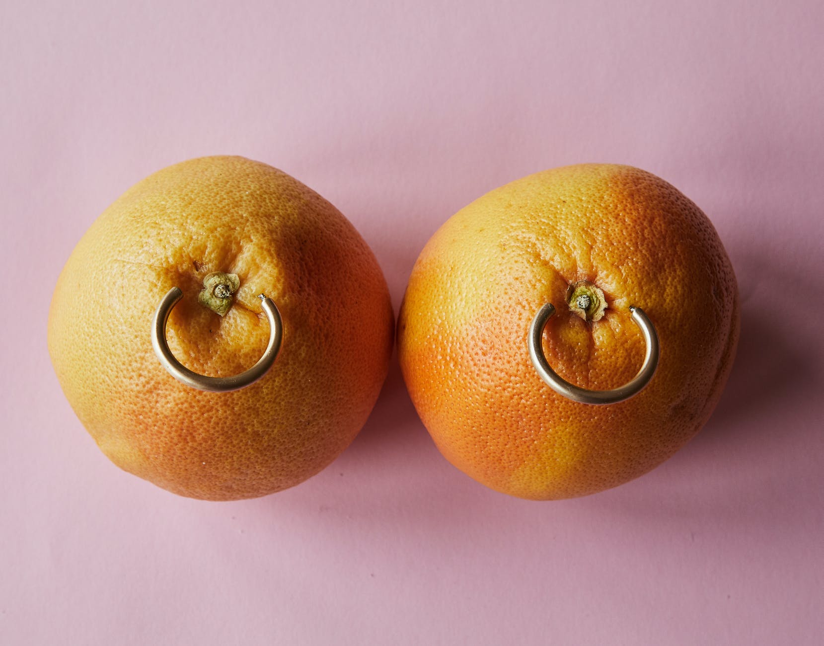 fresh mandarins with earrings placed on pink surface